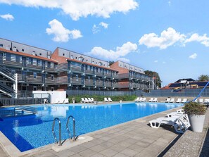 A swimming pool with lounge chairs and a building with multiple balconies in the background. - 6 Person Holiday Home on a Holiday Park in Faaborg (Faaborg)