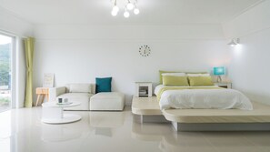 A modern hotel room with a sofa, a bed, a bedside table, a lamp, and a wall clock. - Daebudo Aladdin Pension (Ansan)
