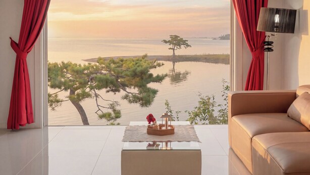 A room with a large window, a sofa, a small table with a decorative item, and red curtains. - Daebudo Aladdin Pension (Ansan)