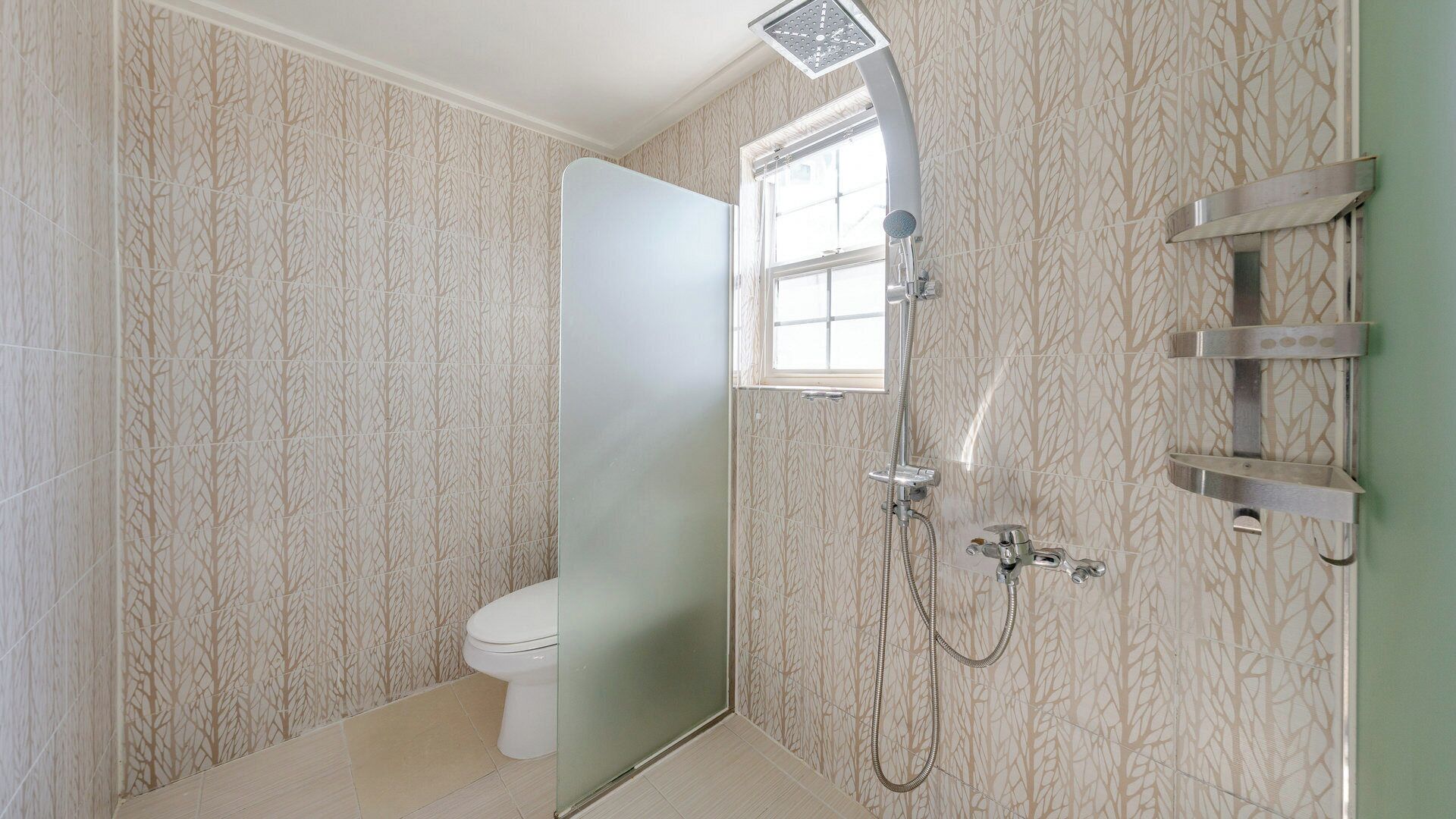 A bathroom with a toilet, a shower with a handheld showerhead, and a window.