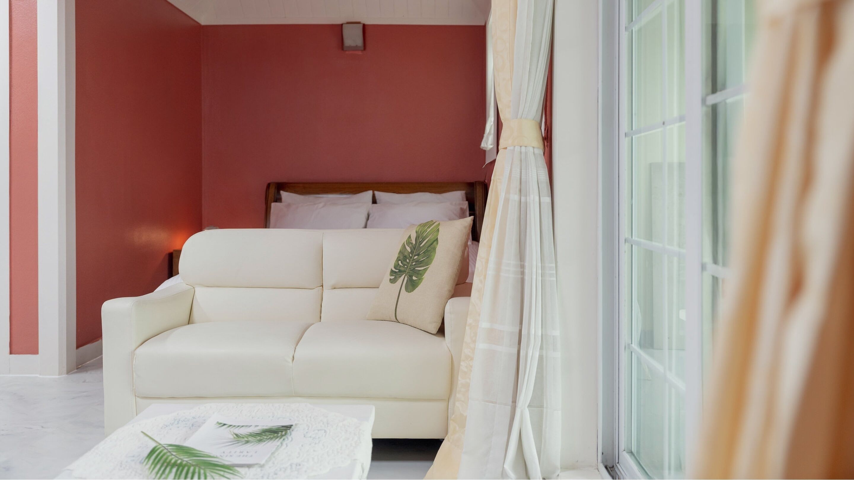 Una habitación acogedora con un sofá blanco, una mesita con una planta y una cama con ropa de cama blanca.