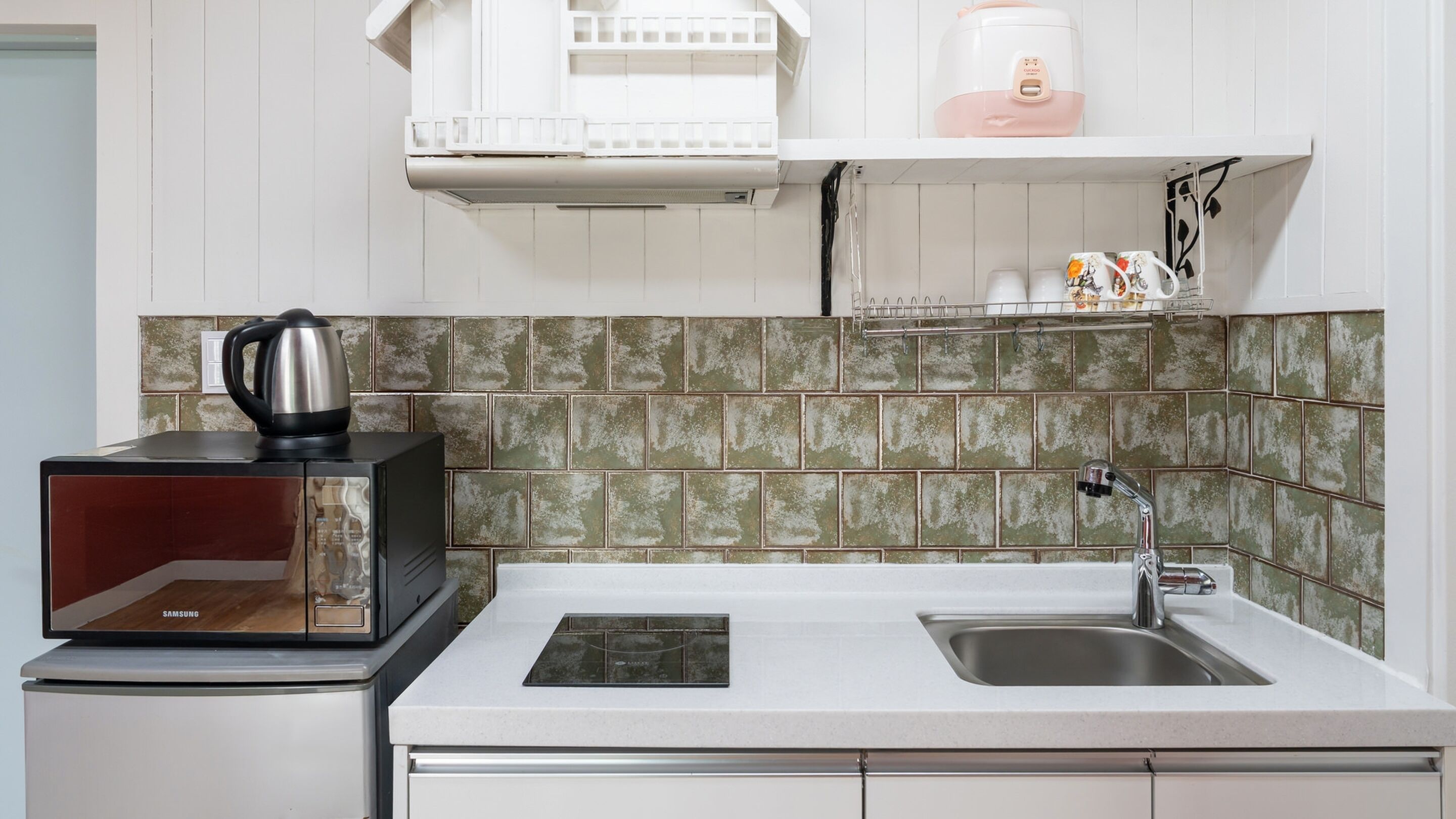 A kitchen with a microwave, kettle, and sink.