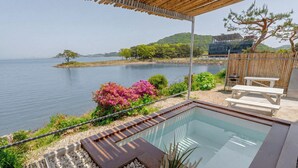 A pool with a wooden deck, a covered seating area, and a view of the water and hills. - Daebudo Aladdin Pension (Ansan)