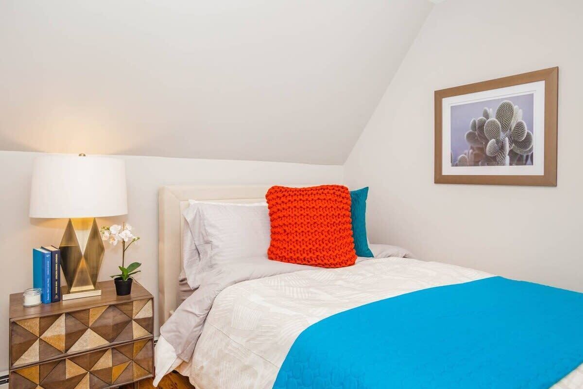 Quarto bem arrumado com cama, travesseiros, mesa de cabeceira com abajur e um quadro na parede.