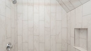 A bathroom with white marble tiles, a showerhead, and a small shelf. - Charming Boston Home | Near T (Boston)