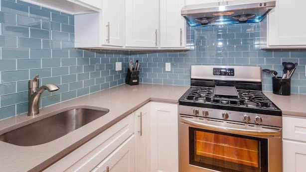 A kitchen with white cabinets, a stainless steel sink, a gas stove, and a built-in oven. - Charming Boston Home | Near T (Boston)