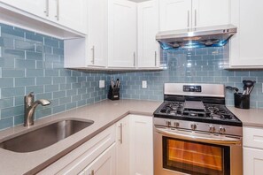 A kitchen with white cabinets, a stainless steel sink, a gas stove, and a built-in oven. - Charming Boston Home | Near T (Boston)