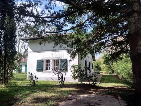 A small, white building with a sloped roof, surrounded by trees and grass.