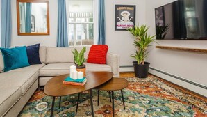 A living room with a sofa, a coffee table with books and candles, a TV, and two potted plants. - Bright & Spacious Boston Home | near T (Boston)