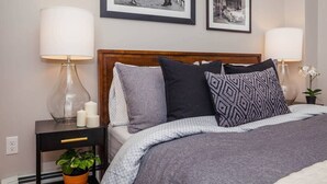 A neatly arranged bedroom with a wooden headboard, a bed with patterned bedding, two bedside tables with lamps, and framed black and white photographs on the wall. - Bright & Spacious Boston Home | near T (Boston)