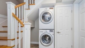 A laundry room with two stacked front-loading washing machines, a white door, and a wooden staircase. - Bright & Spacious Boston Home | near T (Boston)