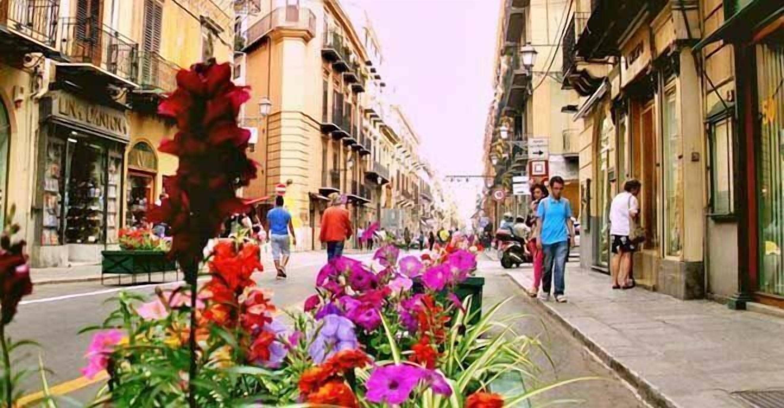 Uma rua ladeada por edifícios, com calçada e pessoas caminhando.