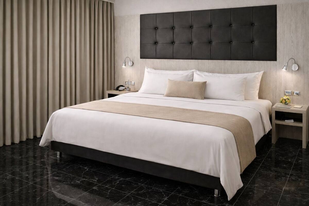 A modern hotel room with a large bed, dark headboard, and two bedside tables with lamps.