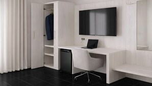 A modern hotel room with a white desk, a flat-screen TV, a laptop, a white chair, and a built-in dishwasher.