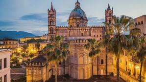 A historic cathedral with a large dome and two bell towers, surrounded by palm trees and other buildings.