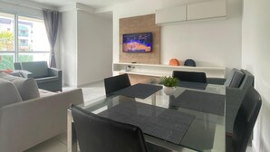 Ein modernes Wohnzimmer mit einem Glastisch, schwarzen Stühlen, einem weißen Sofa und einem an der Wand montierten Fernseher.