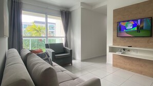 Ein modernes Wohnzimmer mit einer Couch, einem an der Wand befestigten Fernseher und einem Fenster mit Vorhängen.