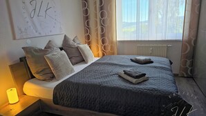 A bedroom with a bed, pillows, a bedside table with a lamp, a window with curtains, and a wall with a poster. - ErzZeit - Vacation with a vision (Schwarzenberg/Erzgebirge)