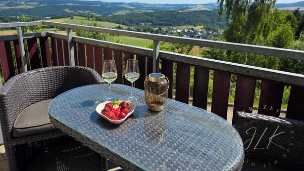 A balcony with wicker furniture, two wine glasses, a bowl of strawberries, and a thermos. - ErzZeit - Vacation with a vision (Schwarzenberg/Erzgebirge)