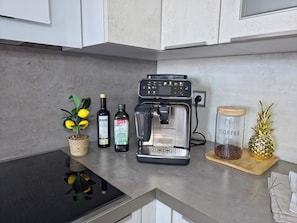 A kitchen counter with a coffee maker, a jar of coffee beans, a bottle of olive oil, and a decorative pineapple.