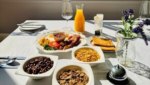 A breakfast table with various dishes, a glass of orange juice, and a view of a garden through a window. - Dwaleni Farm Lodge (Matsapha)