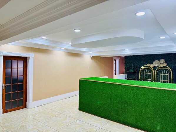 A reception area with a green artificial grass partition, beige walls, and a wooden door.