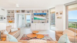 Ett rymligt vardagsrum med en stor TV, bekväma sittplatser och utsikt över stranden.