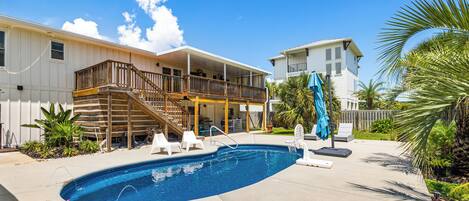 A backyard with a swimming pool, a wooden deck, and a covered patio area.