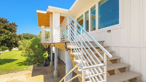 A modern house with a wooden deck, a staircase with metal railings, and a clear view of the surrounding greenery. - Spacious Pensacola Beach Retreat with Private Pool & Game Room | Sleeps 15 (Pensacola Beach)