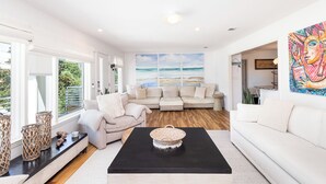 A spacious living room with a large window, a black coffee table, and a beige sofa. - Spacious Pensacola Beach Retreat with Private Pool & Game Room | Sleeps 15 (Pensacola Beach)
