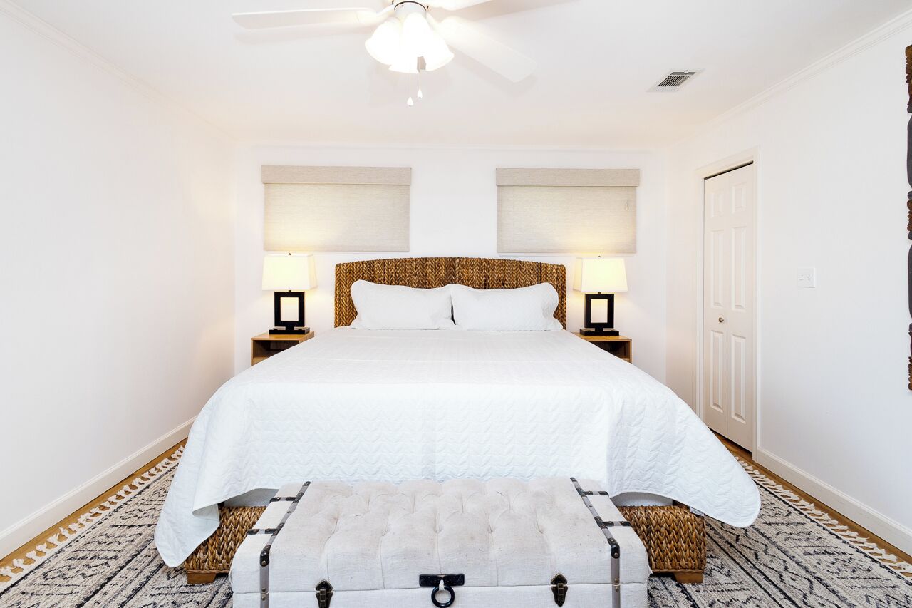A neatly arranged bedroom with a large bed, two bedside lamps, a ceiling fan, and a patterned rug.