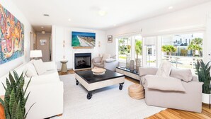 A modern living room with a fireplace, white sofas, a coffee table, and large windows offering a view of the city. - Spacious Pensacola Beach Retreat with Private Pool & Game Room | Sleeps 15 (Pensacola Beach)