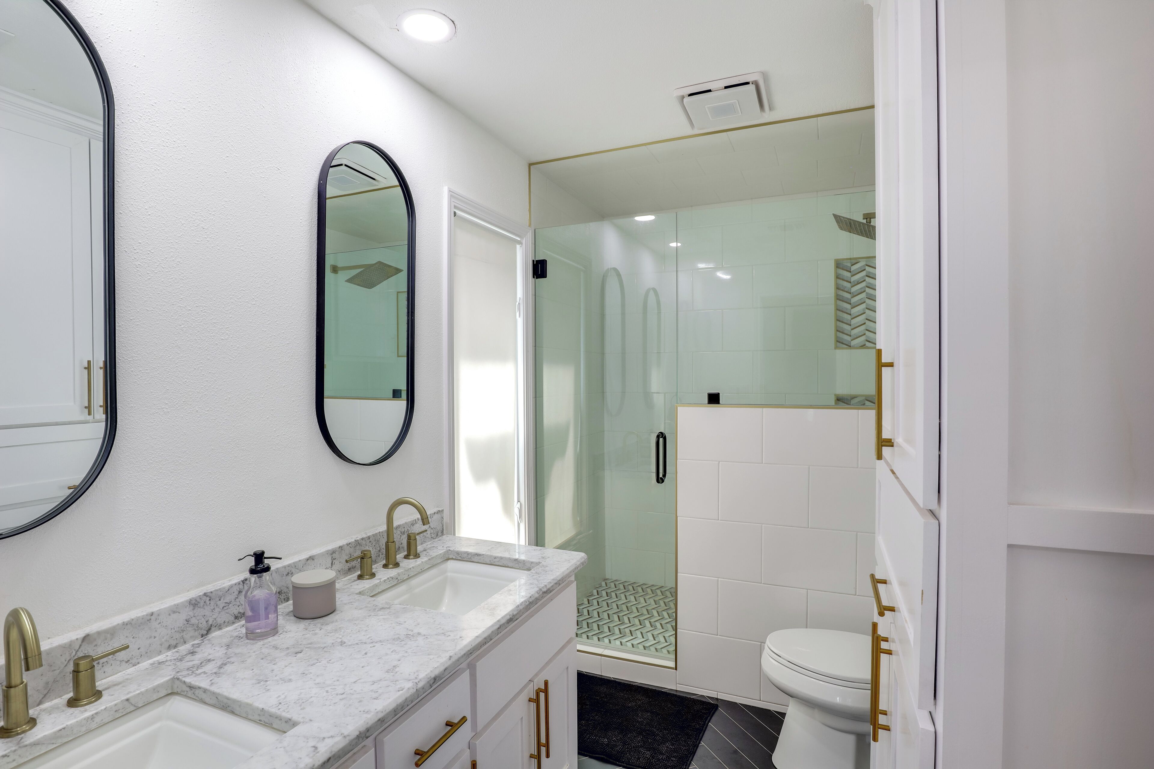 Une salle de bain moderne avec un comptoir en marbre, un grand miroir, une douche en verre et des toilettes dotées de poignées dorées.