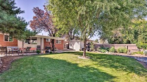 A residential backyard with a lawn, a small tree, and a brick house with a patio area. - Modern Salt Lake City Apt.- 20mi to Snowbird! (Salt Lake City)