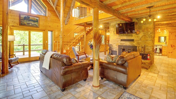 A spacious living area with leather sofas, a stone fireplace, and a wooden staircase. - 3,000 Sq Ft + Game Room: Ozarks Serenity Cabin! (Harrison)