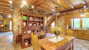 A rustic wooden interior with a dining table, wooden cabinets, and a stone wall. - 3,000 Sq Ft + Game Room: Ozarks Serenity Cabin! (Harrison)