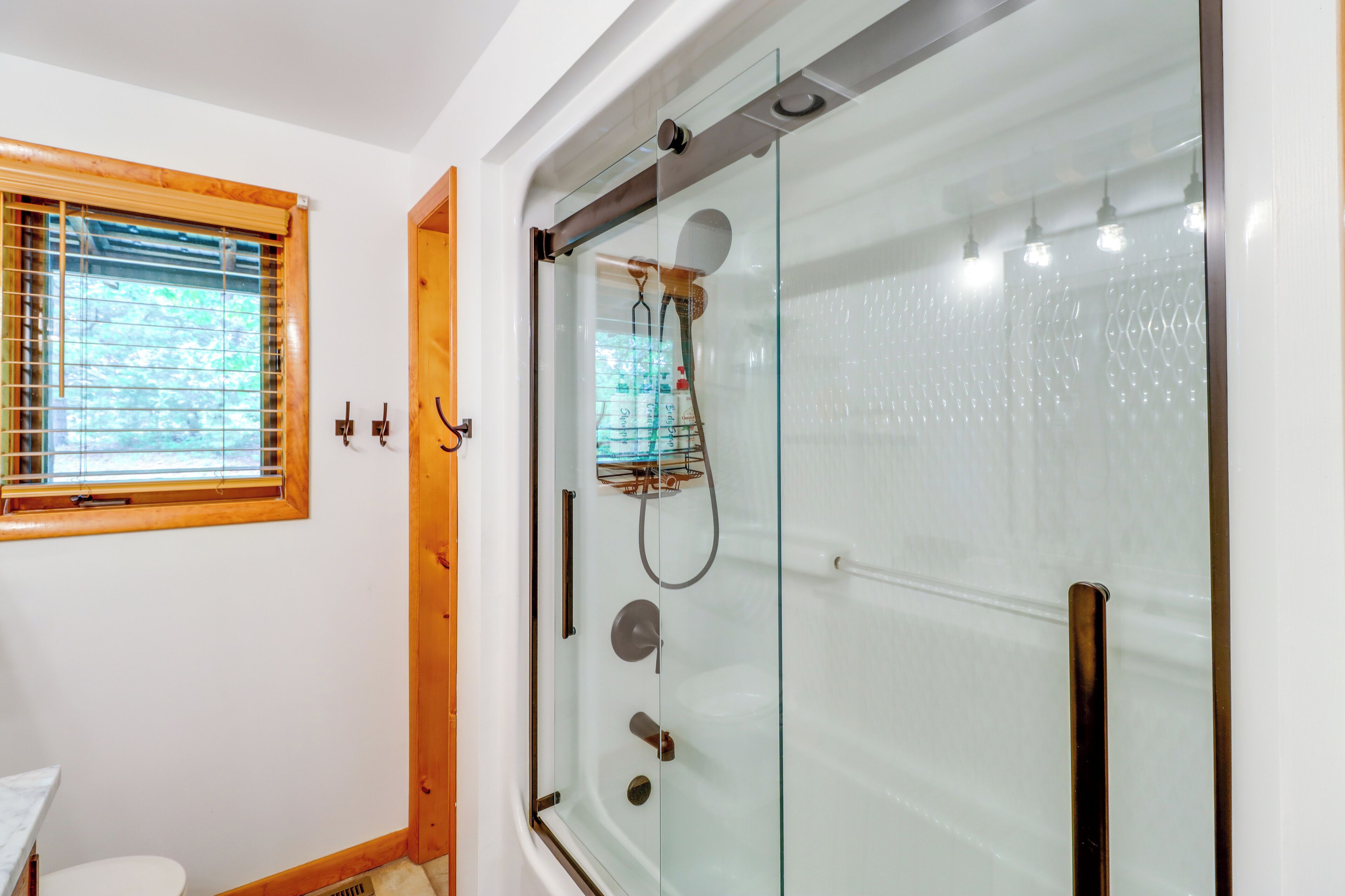 Un baño con ducha de vidrio, una ventana con persianas y un inodoro.