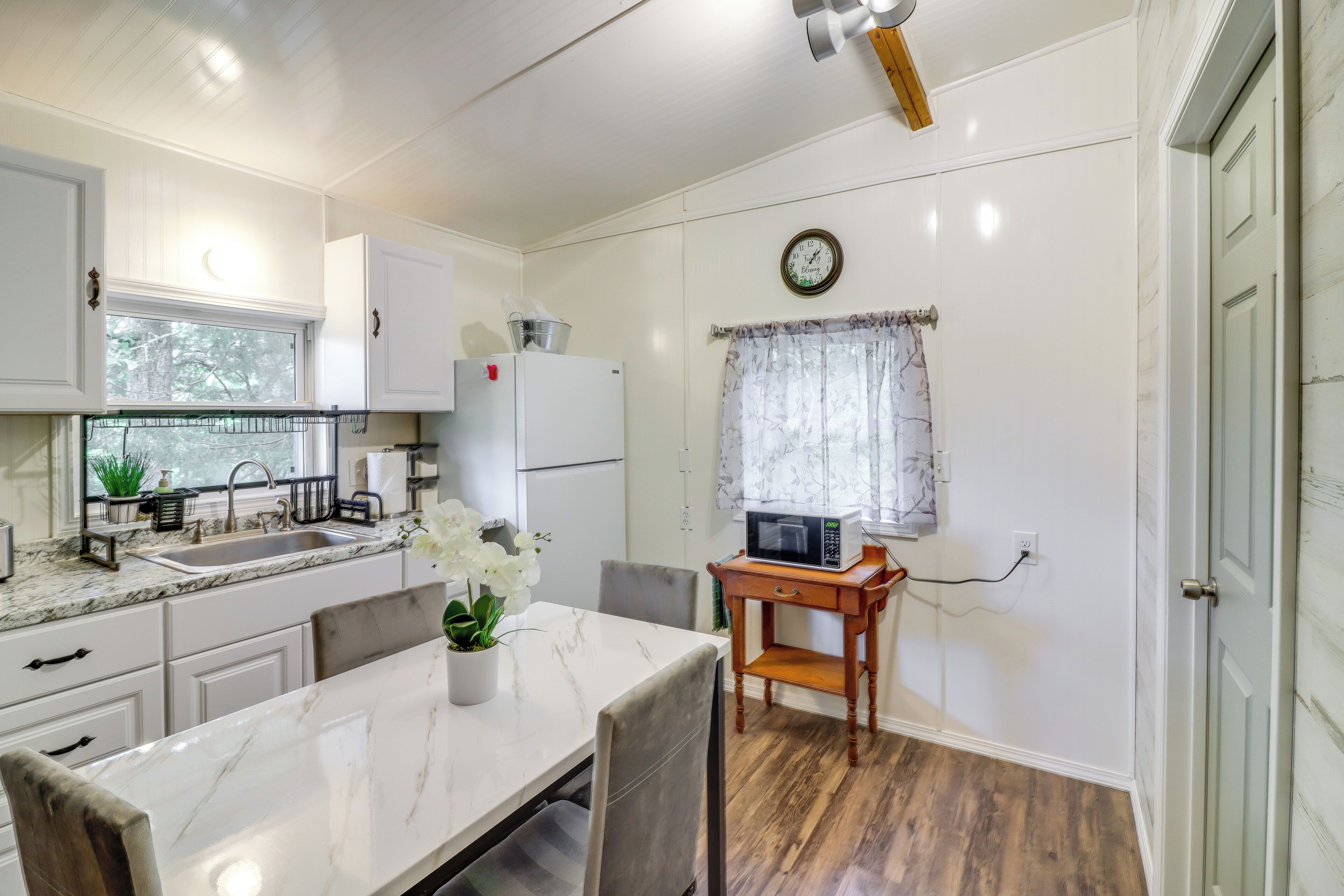 A compact kitchen with white cabinets, a sink, a microwave, and a dining area with a table and chairs.