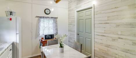 Una cocina compacta con encimera de mármol blanco, microondas y comedor con mesa y sillas blancas.