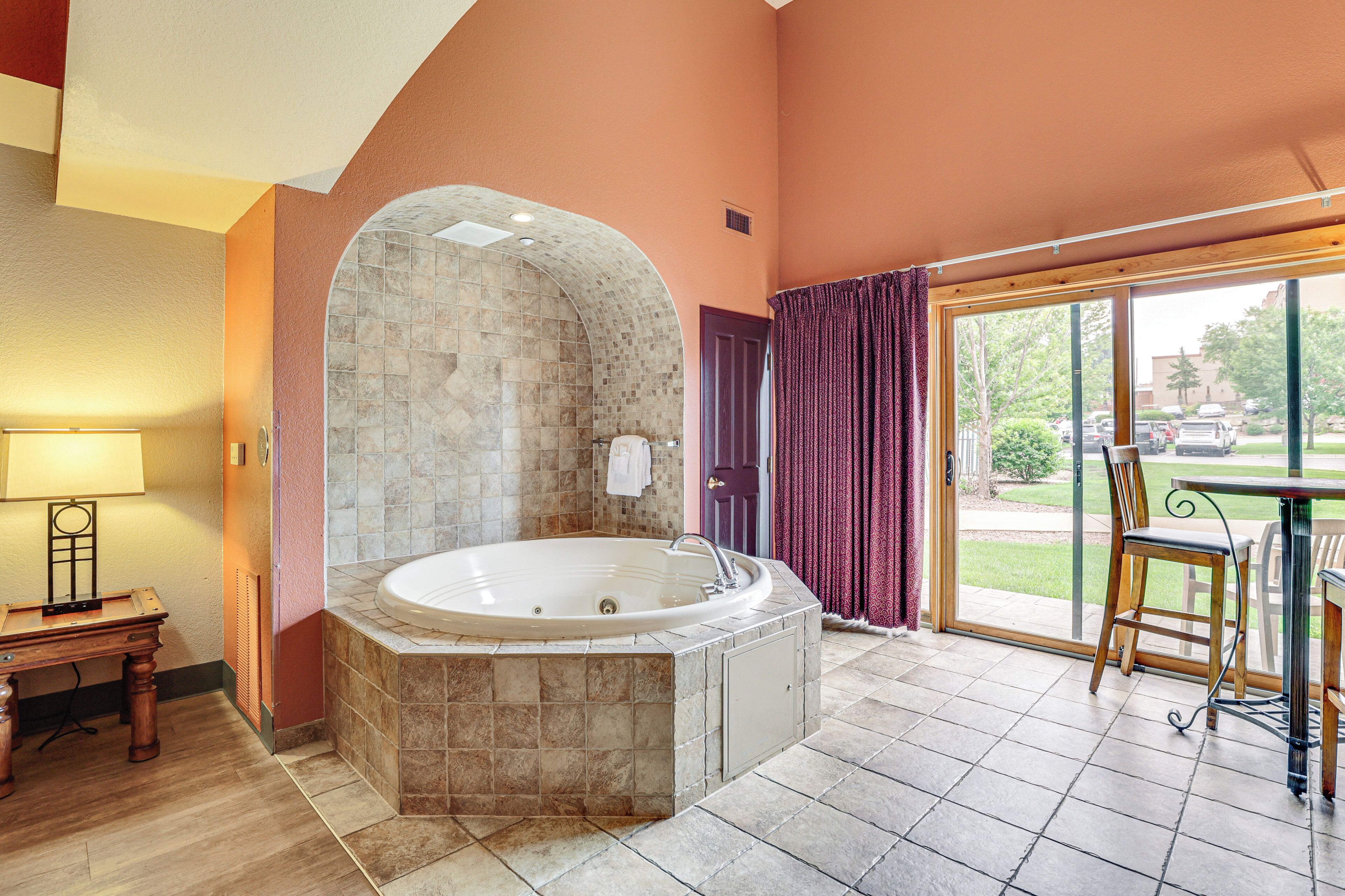 A bathroom with a stone bathtub, a wooden table with chairs, and a view of the outdoors through a glass door.
