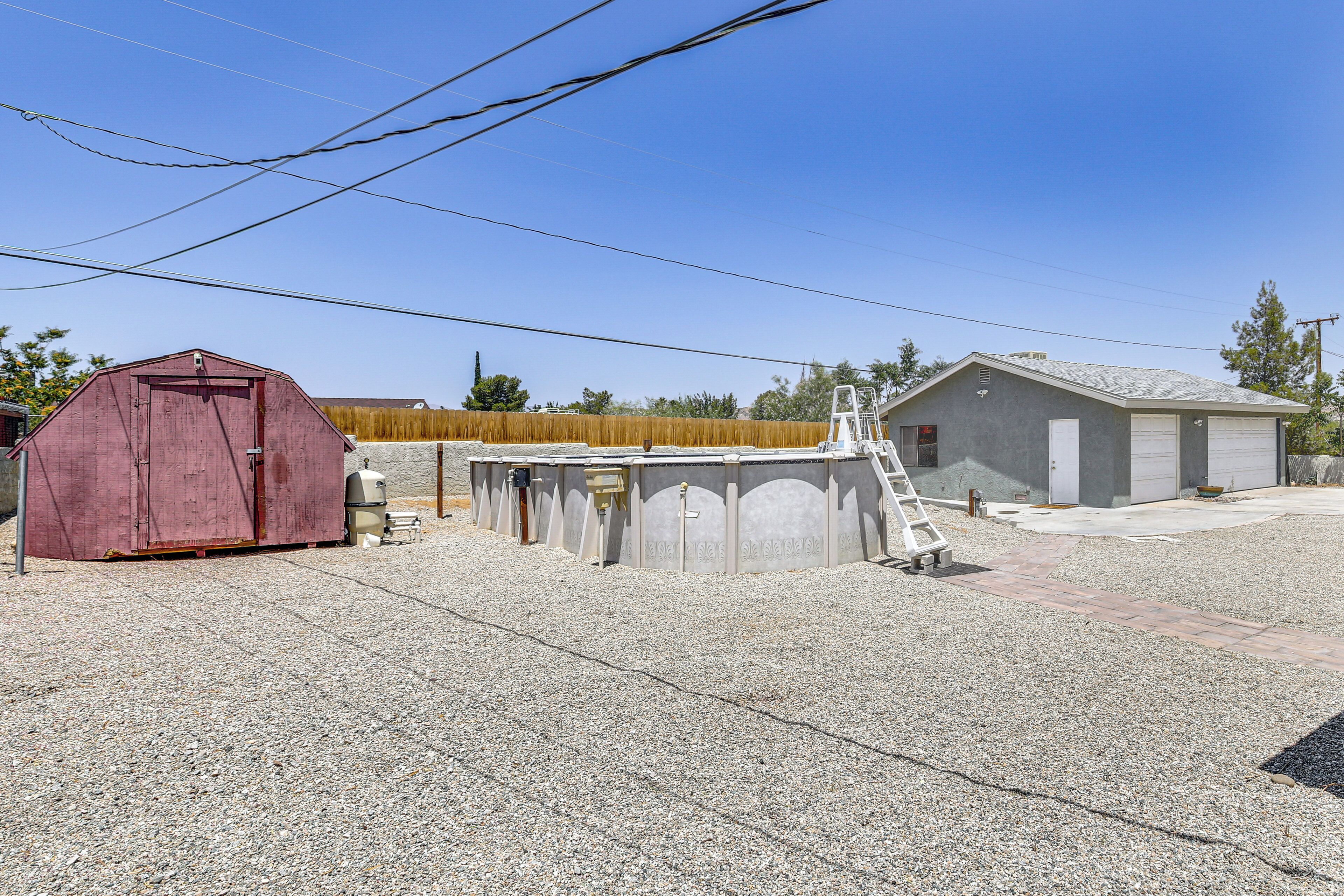 A gravel driveway leading to a garage with a ladder, a red shed, and a small building with a garage door.