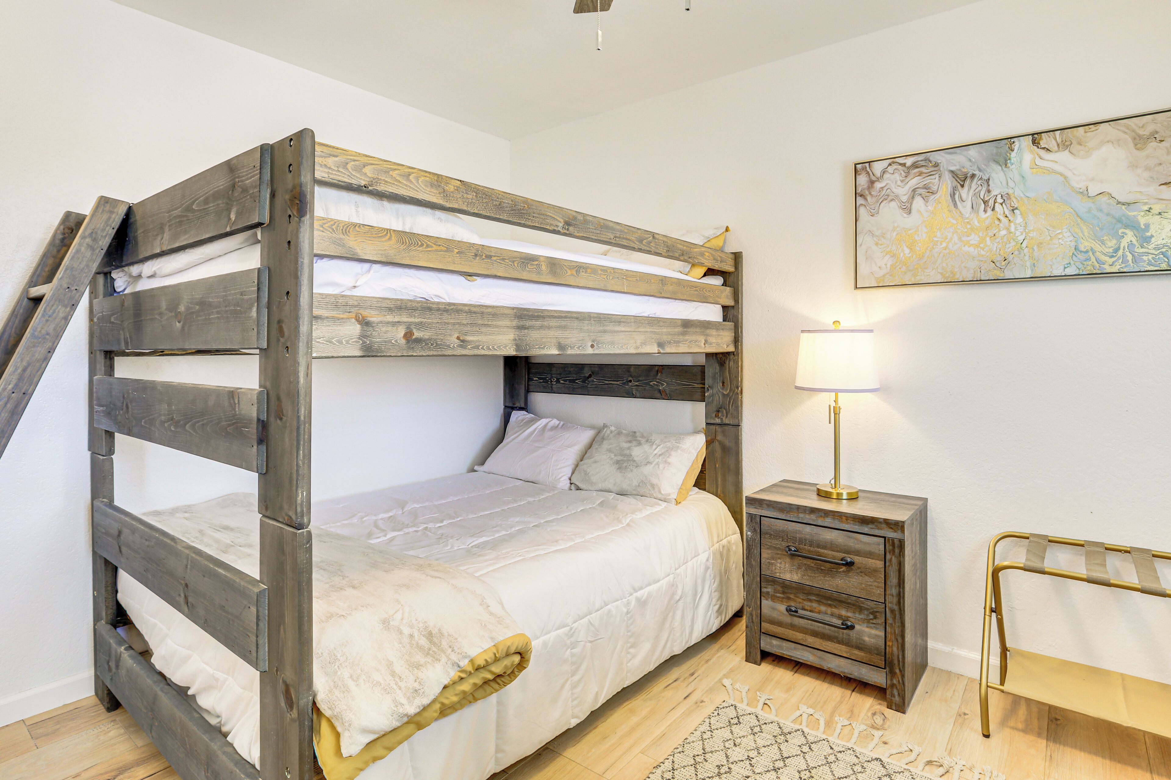 A bunk bed with a ladder, a bedside table with drawers, a lamp, and a rug.