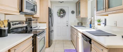 Una cocina moderna con electrodomésticos de acero inoxidable, armarios de madera y una encimera blanca.
