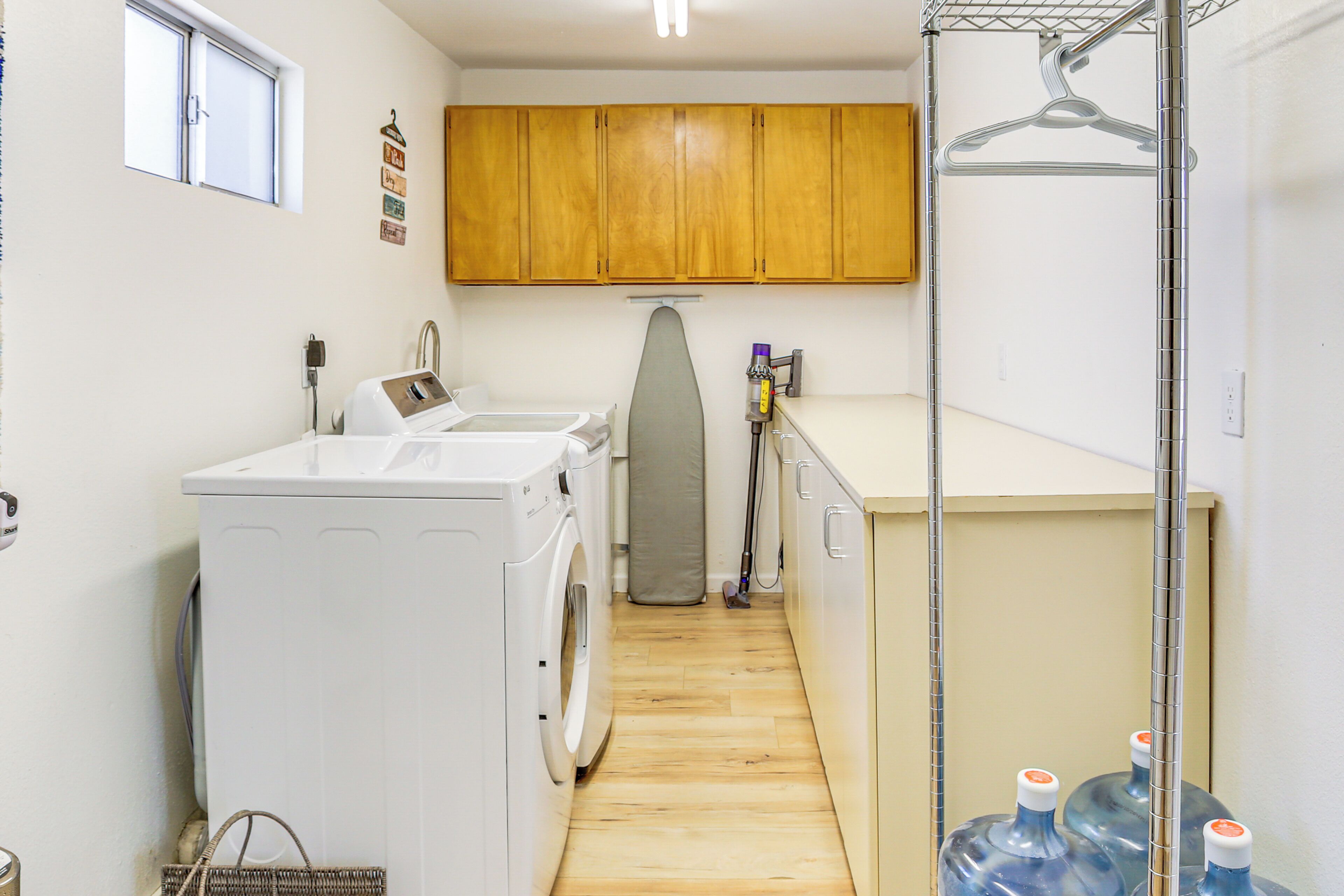 A laundry room with a washing machine, dryer, ironing board, and large water jugs.