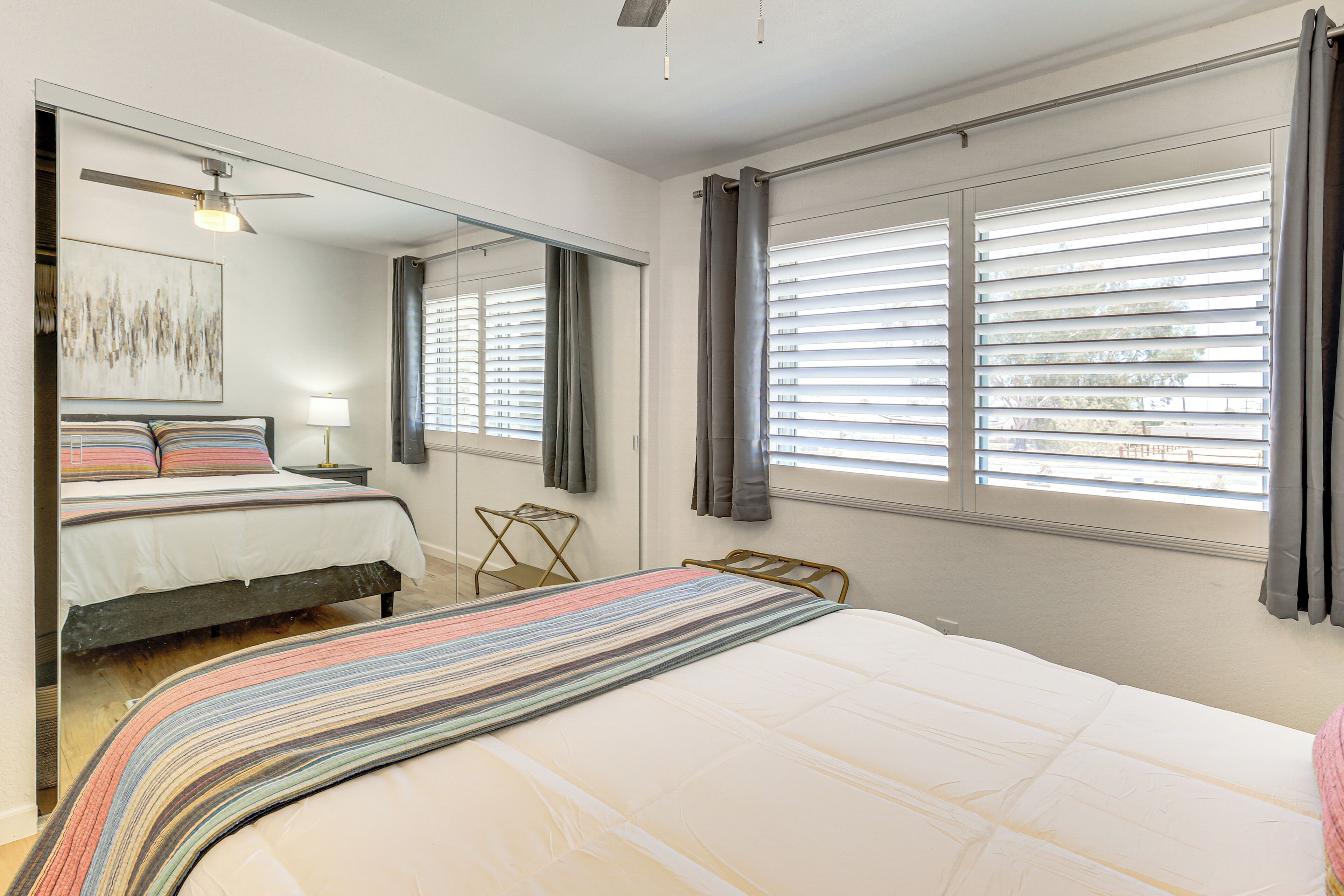 A bedroom with a large bed, a bedside table, a mirror, and a window with blinds.