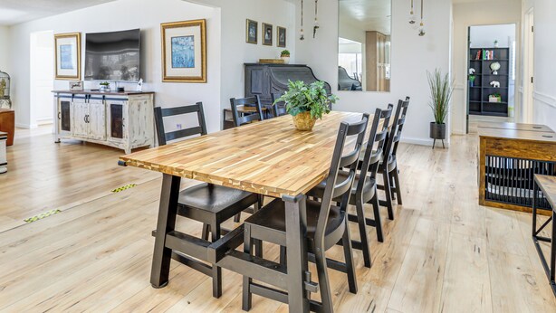 A modern dining area with a wooden table and chairs, a potted plant, and a kitchen in the background. - 9 Mi to Joshua Tree NP: Yucca Valley Home w/ Pool (Yucca Valley)