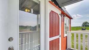 Une porte en bois avec une fenêtre, une rambarde de véranda blanche et un ciel dégagé en arrière-plan.
