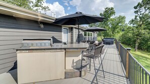 An outdoor deck with a grill, bar area, and outdoor seating. - Outdoor Kitchen + Hot Tub: Table Rock Lake House (Golden)