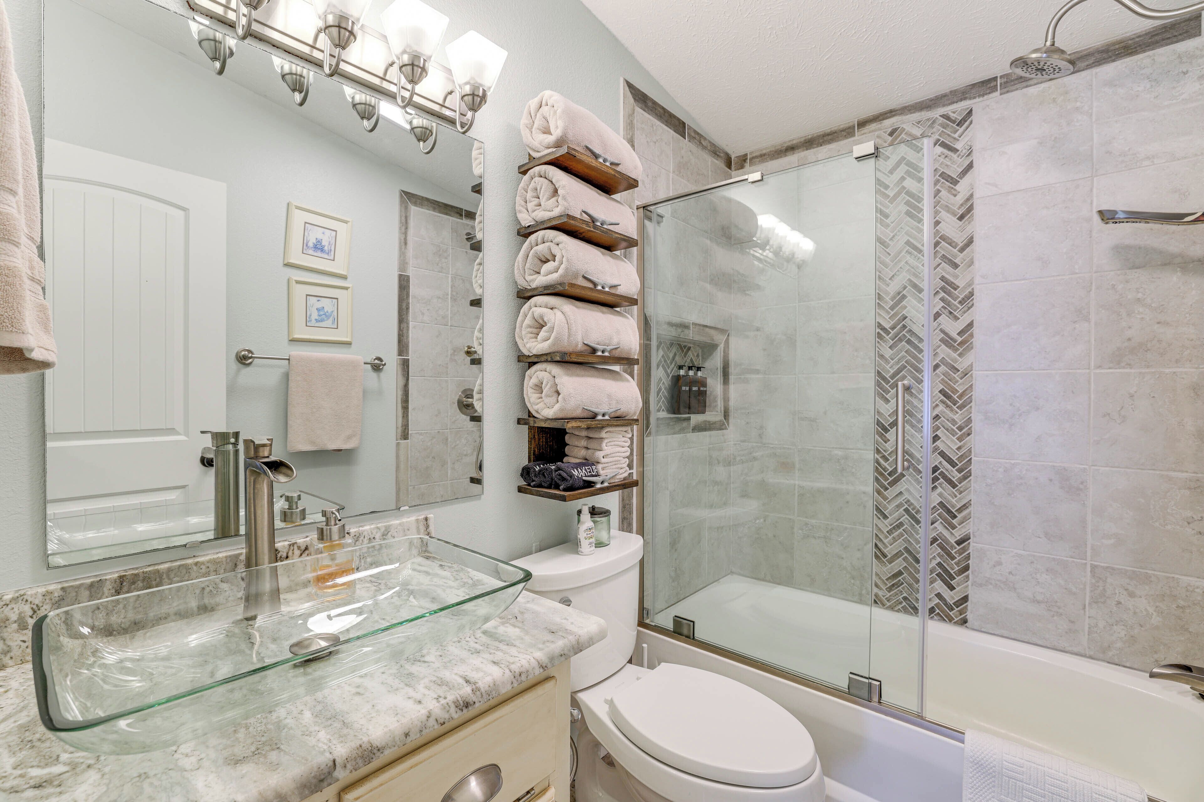 Ein modernes Badezimmer mit Waschbecken aus Glas, Toilette, Dusche mit Glastür und Handtuchhalter mit ordentlich gefalteten Handtüchern.