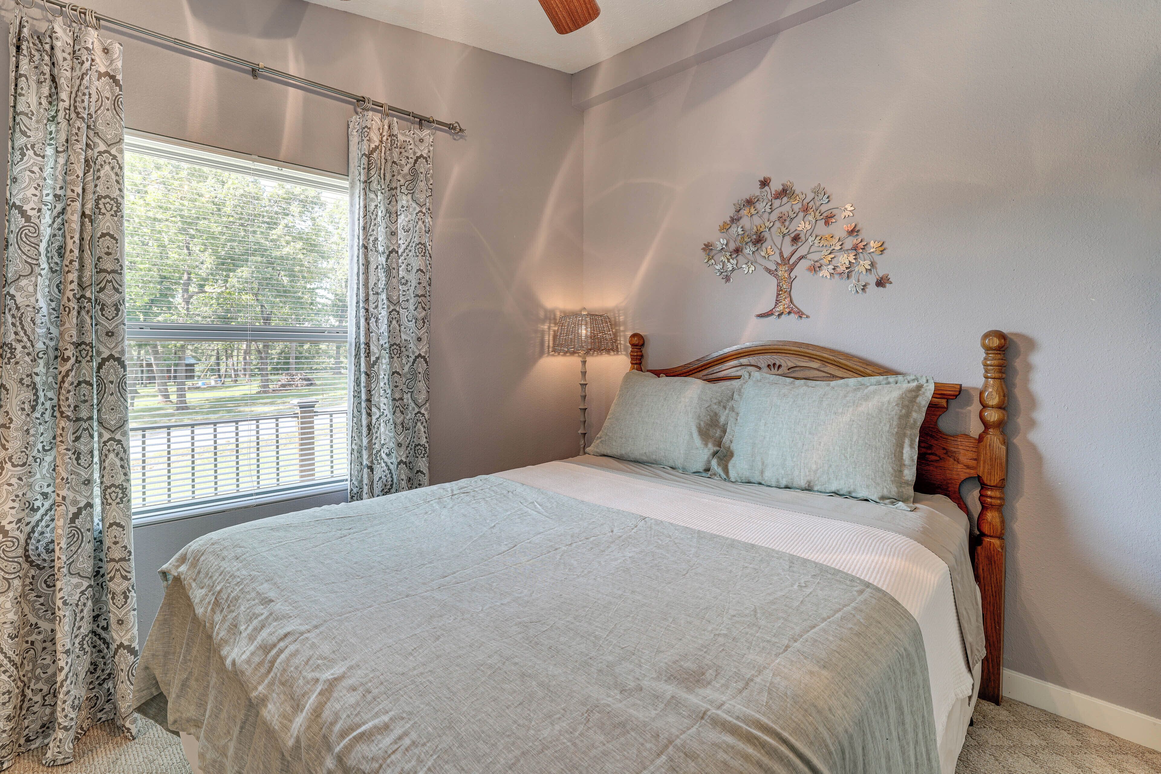 Een slaapkamer met een groot bed, een raam met gordijnen, een wandlamp en een decoratieve boom aan de muur.